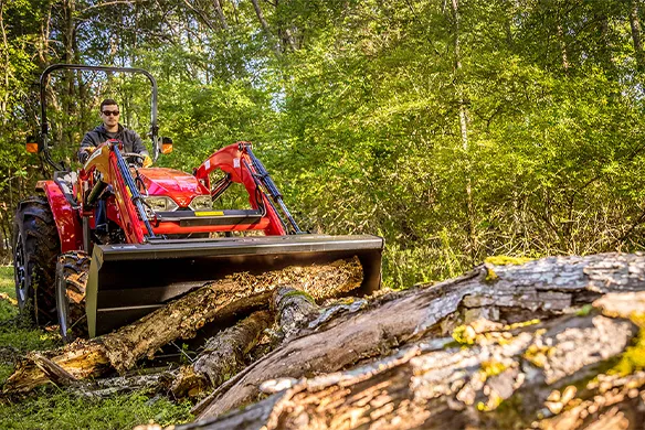 Massey Ferguson compact tractor working in a forest to clear logs from trail.